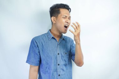 Genç yakışıklı adam izole edilmiş arka planda esniyor ve elleriyle ağzını kapatıyor.