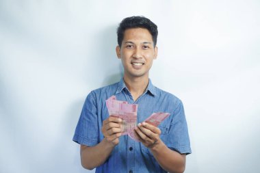 Asyalı yakışıklı adam elinde yüzbinlerce rupiah banknotuyla gururla bağırıyor zaferi ve başarıyı kutluyor.