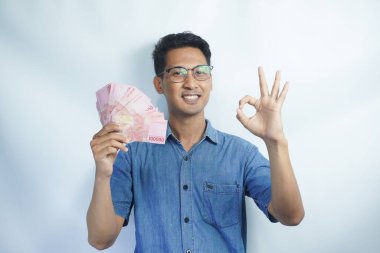 Asyalı yakışıklı adam elinde yüzbinlerce rupiah banknotuyla gururla bağırıyor zaferi ve başarıyı kutluyor.