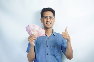 Asyalı yakışıklı adam elinde yüzbinlerce rupiah banknotuyla gururla bağırıyor zaferi ve başarıyı kutluyor.