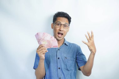 Asyalı yakışıklı adam elinde yüzbinlerce rupiah banknotuyla gururla bağırıyor zaferi ve başarıyı kutluyor.