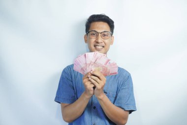 Asyalı yakışıklı adam elinde yüzbinlerce rupiah banknotuyla gururla bağırıyor zaferi ve başarıyı kutluyor.