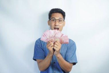 Asyalı yakışıklı adam elinde yüzbinlerce rupiah banknotuyla gururla bağırıyor zaferi ve başarıyı kutluyor.