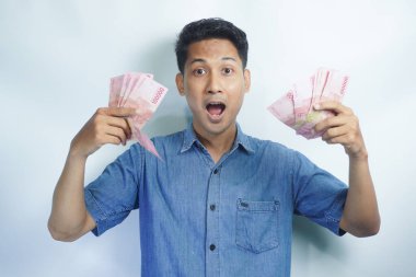 Asyalı yakışıklı adam elinde yüzbinlerce rupiah banknotuyla gururla bağırıyor zaferi ve başarıyı kutluyor.