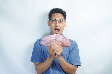 Asyalı yakışıklı adam elinde yüzbinlerce rupiah banknotuyla gururla bağırıyor zaferi ve başarıyı kutluyor.