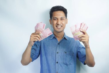 Asyalı yakışıklı adam elinde yüzbinlerce rupiah banknotuyla gururla bağırıyor zaferi ve başarıyı kutluyor.