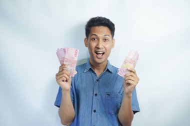 Asyalı yakışıklı adam elinde yüzbinlerce rupiah banknotuyla gururla bağırıyor zaferi ve başarıyı kutluyor.