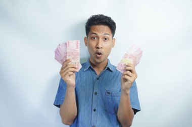 Asyalı yakışıklı adam elinde yüzbinlerce rupiah banknotuyla gururla bağırıyor zaferi ve başarıyı kutluyor.
