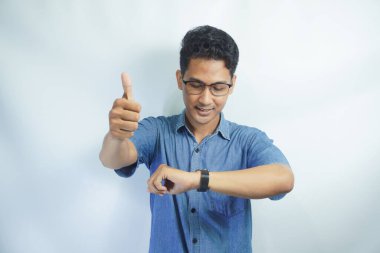 Mavi tişörtlü Asyalı bir adamın portresi beyaz arka plandaki saatine bakarak gülümsüyor.