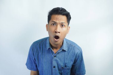 Mavi gömlekli genç Asyalı adamın portresi beyaz arka planda ağzını açtığı için şok oldu.