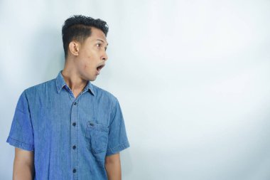 Mavi gömlekli genç Asyalı adamın portresi beyaz arka planda ağzını açtığı için şok oldu.