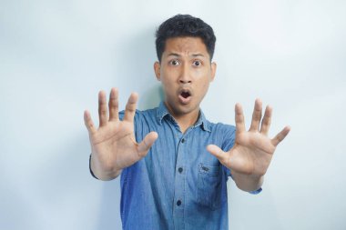 İzole edilmiş beyaz arka plandaki çekici Asyalı genç adam korkmuş ve korkmuş ifadeyle dehşete düşmüş. Ellerinle hareket etmeyi kes, şok içinde çığlık atmayı kes. Panik konsepti.