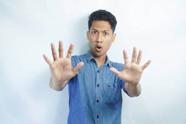 İzole edilmiş beyaz arka plandaki çekici Asyalı genç adam korkmuş ve korkmuş ifadeyle dehşete düşmüş. Ellerinle hareket etmeyi kes, şok içinde çığlık atmayı kes. Panik konsepti.