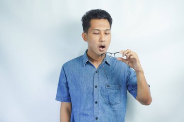 Mavi gömlekli Asyalı genç adam onun gözlüklerini üflüyor ve temizliyor. beyaz üzerine izole