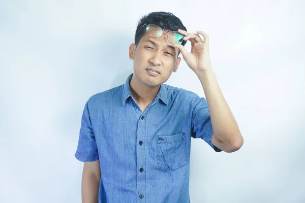 Asian young man wearing blue shirt taking off the glasses to see far away