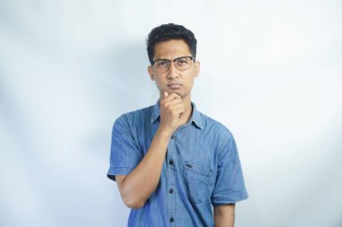 Düşünmem gerek. Mavi gömlekli Asyalı bir adamın portresi. Çenesini tutuyor ve bir fikir üzerinde kafa yoruyor. Çözüm konusunda kafası karışık. Beyaz arka planda izole edilmiş kapalı stüdyo çekimi