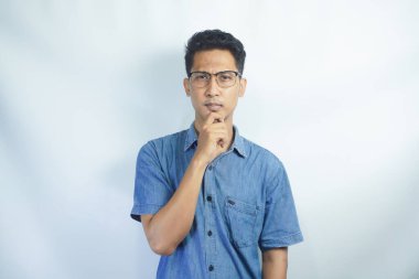Düşünmem gerek. Mavi gömlekli Asyalı bir adamın portresi. Çenesini tutuyor ve bir fikir üzerinde kafa yoruyor. Çözüm konusunda kafası karışık. Beyaz arka planda izole edilmiş kapalı stüdyo çekimi