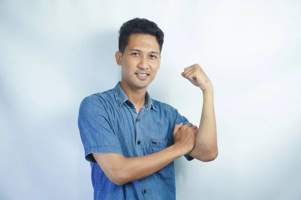 年轻的亚洲男人穿着蓝色的衬衫 站在孤立的白色背景之上 强壮的人表现出臂膀肌肉 自信而自豪 — 图库照片