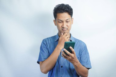 Yetişkin bir Asyalı kafası karışmış bir şekilde elinde tuttuğu cep telefonunu arıyor.