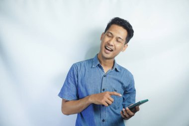 Mutlu ve şaşırmış genç bir adamın görüntüsü cep telefonu kullanarak beyaz duvar arkaplanı üzerinde izole edilmiş..