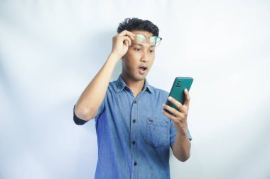 Şok olmuş Asyalı bir adam elinde akıllı telefonu tutuyordu. Gözlükleri havada telefona bakıyordu. Yüzünde şaşkın bir ifade vardı.