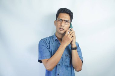 Genç Asyalı adamın telefonu aradığında kafası karışıyor ve şoka giriyor. Endonezyalı adam mavi gömlek giyiyor..