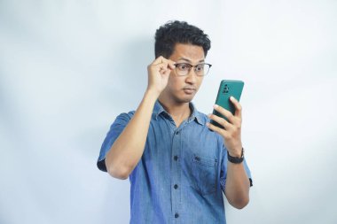 Şok olmuş Asyalı bir adam elinde akıllı telefonu tutuyordu. Gözlükleri havada telefona bakıyordu. Yüzünde şaşkın bir ifade vardı.