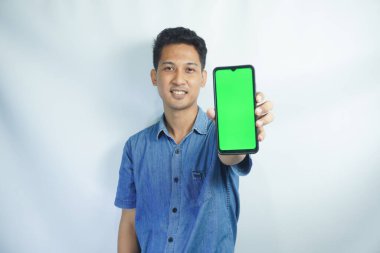 Elinde büyük yeşil ekran akıllı telefon tutan Asyalı bir adamın portresi, cihazı gösteriyor ve işaret ediyor, afiş.