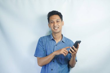 Mutlu ve şaşırmış genç bir adamın görüntüsü cep telefonu kullanarak beyaz duvar arkaplanı üzerinde izole edilmiş..