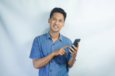 Mutlu ve şaşırmış genç bir adamın görüntüsü cep telefonu kullanarak beyaz duvar arkaplanı üzerinde izole edilmiş..