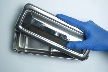 Sağlık görevlileri mavi eldiven takıyor ve ellerinde boş enstrüman tepsisi var.