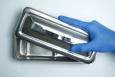 Sağlık görevlileri mavi eldiven takıyor ve ellerinde boş enstrüman tepsisi var.