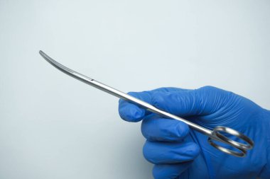 Mavi tıbbi eldiven giyen doktor Necrotomy makaslarını ya da eğri keskin makasları tutar. Bunlar yaranın debridmantasyonunun ana araçlarıdır..