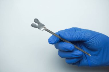 Mavi tıbbi eldiven giyen doktor Yırtık Direktör 'ü tutuyor. Dil ameliyatında dili sabitlemek için kullanılan kelebek uçlu bir sonda. beyaz üzerine izole