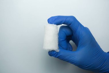 İlk yardım, steril tıbbi pamuk ve hastane acil sağlık konsepti. Beyaz arka planda beyaz sargı bezi rulosu tutan koruyucu lateks eldivenli doktor elleri.