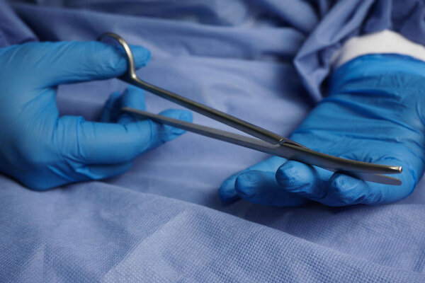 The doctor wearing blue medical gloves holds the Necrotomy Scissors or bent sharp scissors, which are the main instruments in wound debridement.