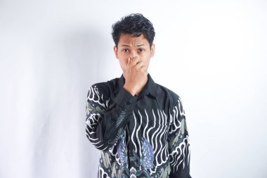 Tiksinmiş Asyalı genç adam elleriyle burnunu kapatıyor.