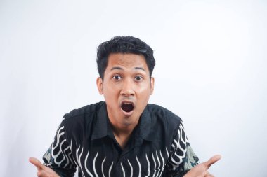 Beyaz arka plan üzerinde duran batik gömlek giyen genç yakışıklı adam şok olmuş yüz ifadesiyle şüpheci ve alaycı görünüyor, ağzı açık kalınca şaşırıyor.