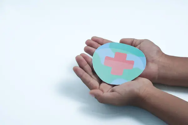 World First Aid Day. Kid hands hold a paper model of the globe with a first aid symbol. Global observance held on the second Saturday in September. World first aid day concept