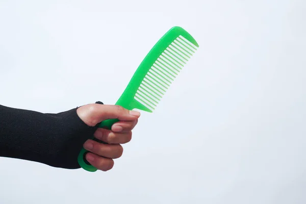 Female hand holding hair accessories green comb over white background, copy space. Set of hairdresser's tools on white background