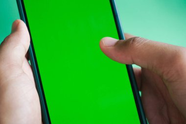 Yeşil ekranlı akıllı telefonu tutan kadın. Yeşil arka planda cep telefonu kullanan bir kadın. Chroma anahtarı, kadın elini dikey yeşil ekranlı telefonla kapat