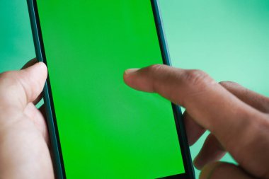 Yeşil ekranlı akıllı telefonu tutan kadın. Yeşil arka planda cep telefonu kullanan bir kadın. Chroma anahtarı, kadın elini dikey yeşil ekranlı telefonla kapat