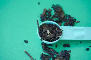 Yeşil arka planda izole edilmiş bir fincan çay yapmak için kaşık içindeki kuru çay yaprakları.