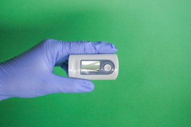 Tıbbi lateks mavi eldivenli bir doktorun sol elinde nabız oksimetresi var. Kandaki oksijen miktarını kontrol etme kavramı