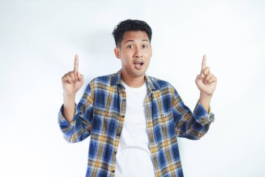 Flanel gömlekli mutlu Endonezyalı adam, kameraya bakıp boş uzayda, izole beyaz arka planda durarak işaret ediyor. Alay konsepti