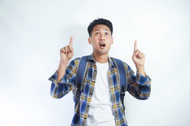 Sırt çantası ve günlük giysiler içinde gülümseyen Asyalı genç bir öğrenci beyaz arka planda izole edilmiş boş bir yeri işaret ediyor. Lise Üniversite Konsepti Eğitimi