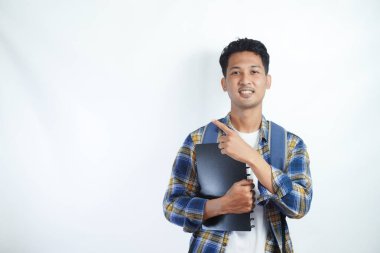 Neşeli Asyalı erkek öğrenci günlük kıyafetler ve sırt çantası gözlükleriyle beyaz arka planda izole edilmiş boş alanı işaret ediyor. Lise üniversite konsepti