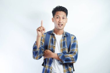 Üniversiteden heyecanlı genç Asyalı erkek öğrenci sırt çantalı, parmakla göstererek beyaz arka planda izole edilmiş bir fikri düşünüyor. Lise üniversite konsepti eğitimi