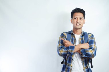 Neşeli Asyalı erkek öğrenci günlük kıyafetler ve sırt çantası gözlükleriyle beyaz arka planda izole edilmiş boş alanı işaret ediyor. Lise üniversite konsepti