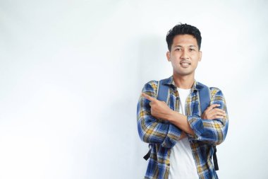 Neşeli Asyalı erkek öğrenci günlük kıyafetler ve sırt çantası gözlükleriyle beyaz arka planda izole edilmiş boş alanı işaret ediyor. Lise üniversite konsepti